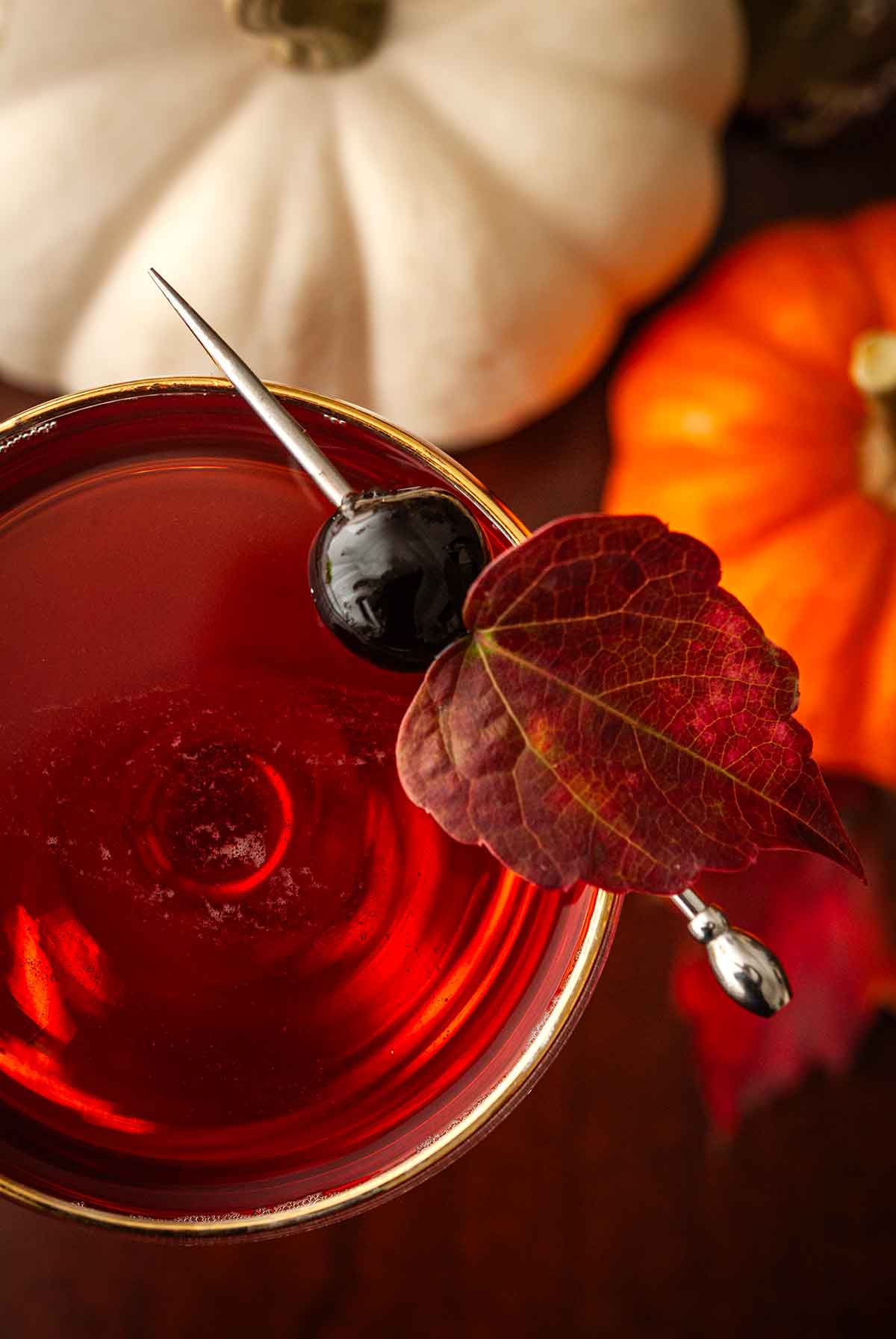 The cherry leaf garnish on a cocktail with pumpkins and leaves beneath it.