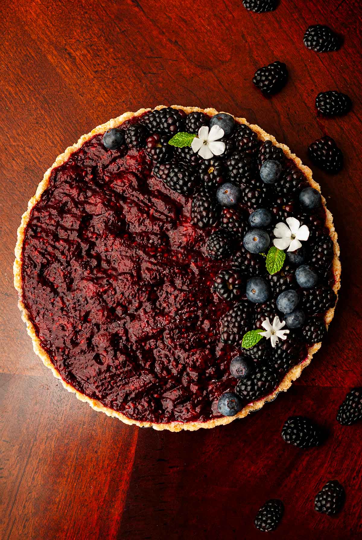 A blackberry Sorel cheesecake on a wooden table, garnished with berries and flowers.