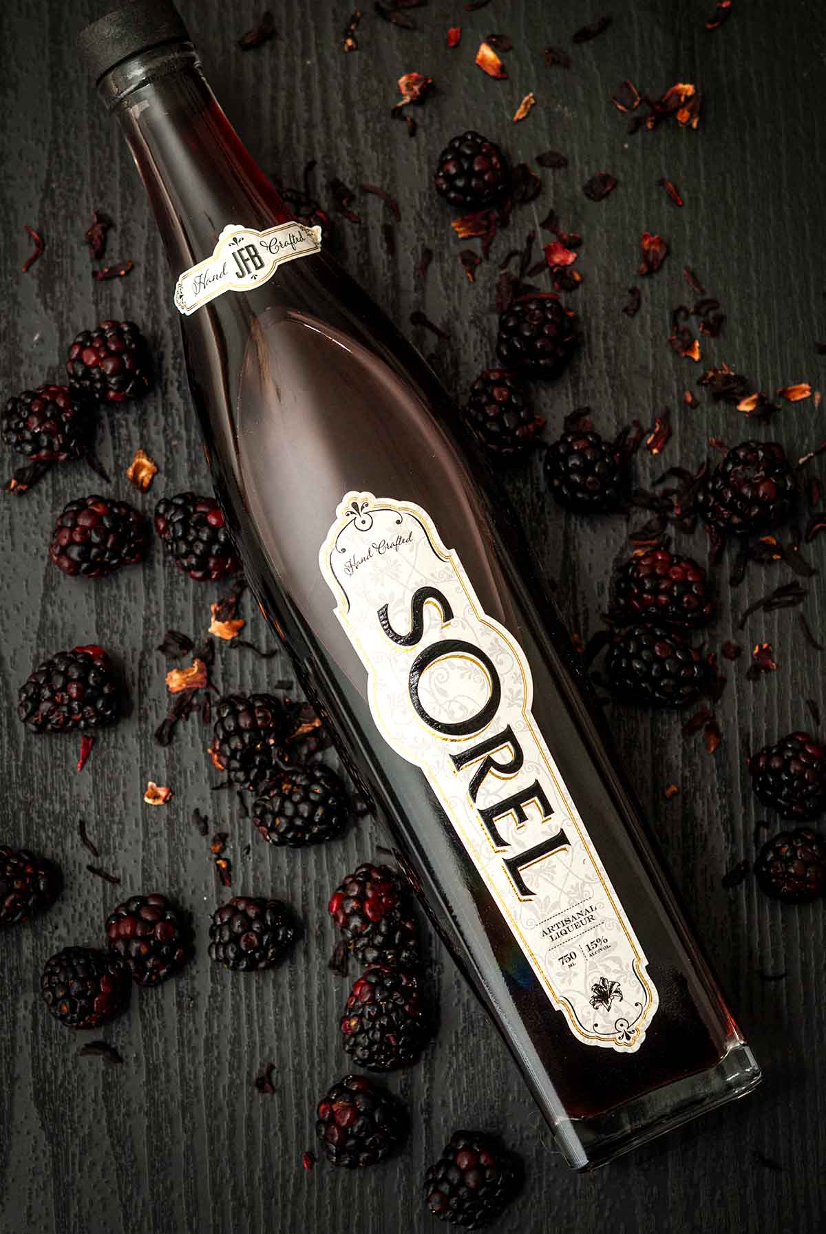 A bottle of Sorel Liqueur on a table, surrounded by blackberries and petals.