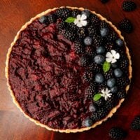 A blackberry Sorel cheesecake on a wooden table, garnished with berries and flowers.