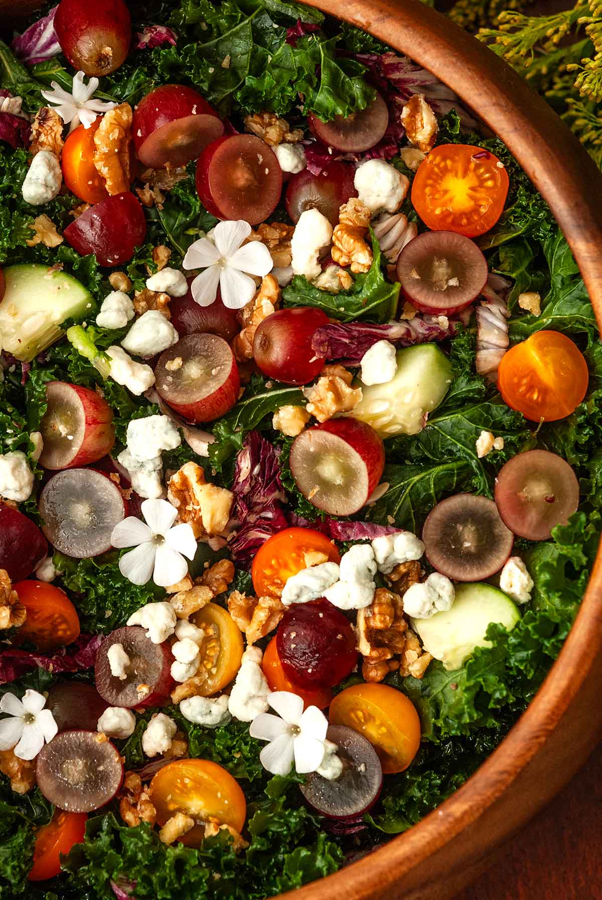 A wooden bowl of salad with grapes with flowers.