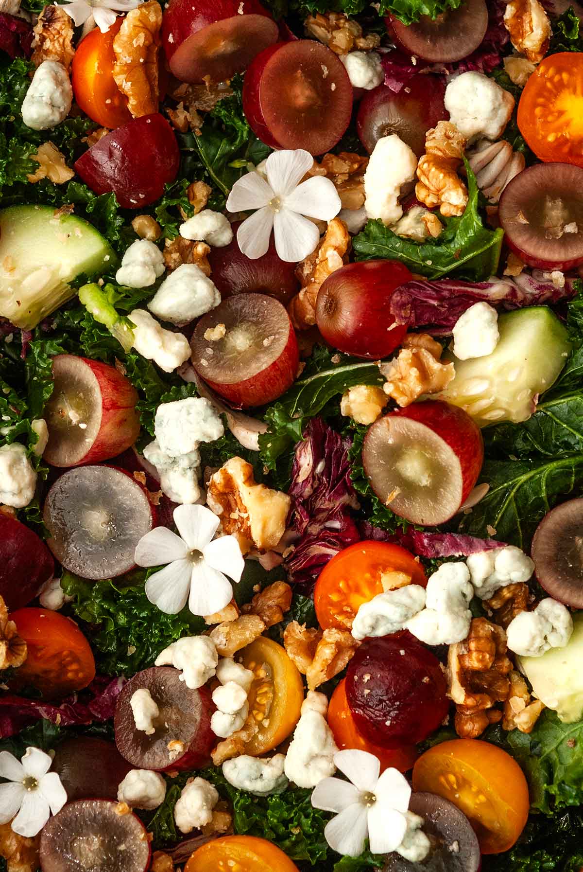 Salad with grapes, tomatoes, cucumbers, walnuts and cheese topped with a few flowers.