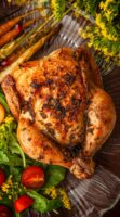 An herbed Cornish game hen on a plate beside flowers, salad and carrots.