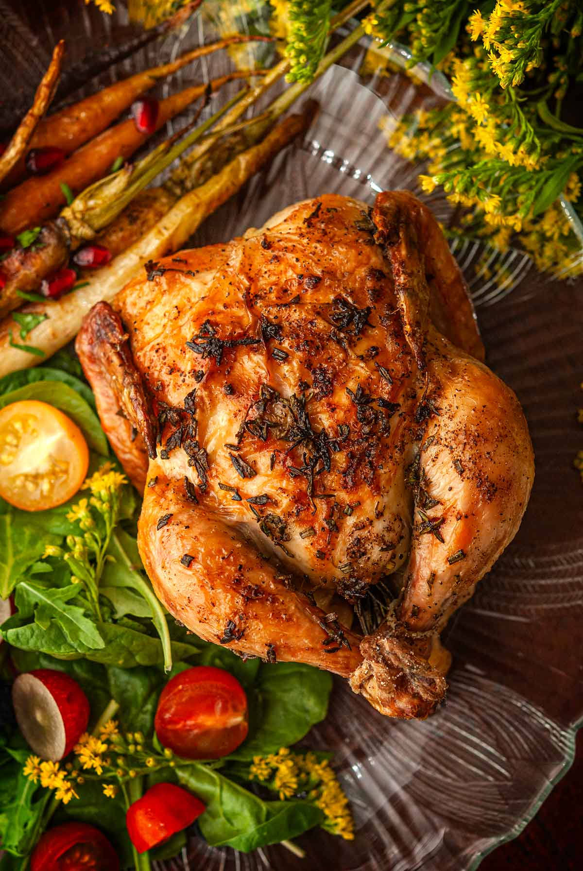 An herbed Cornish game hen on a plate beside flowers, salad and carrots.