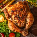 An herbed Cornish game hen on a plate beside flowers, salad and carrots.