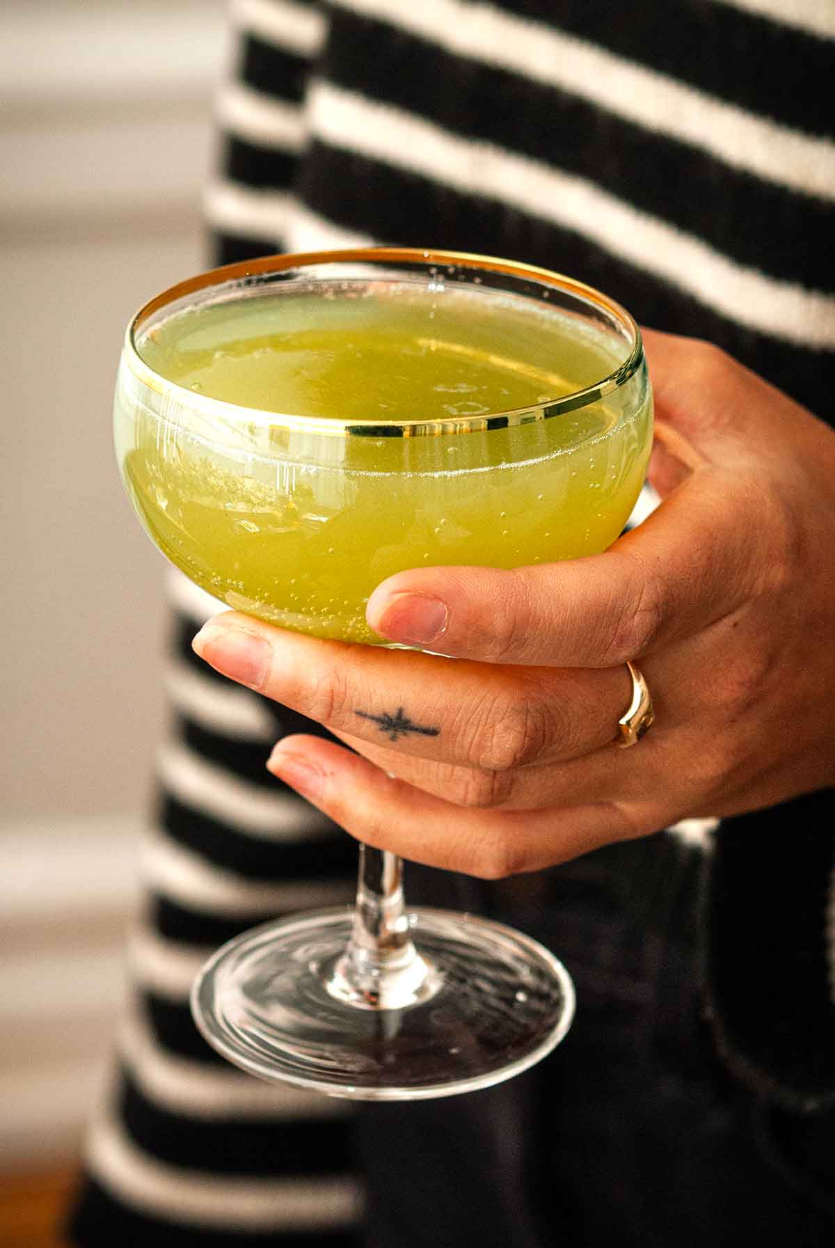 A hand holding a cocktail in a gold-rimmed glass.