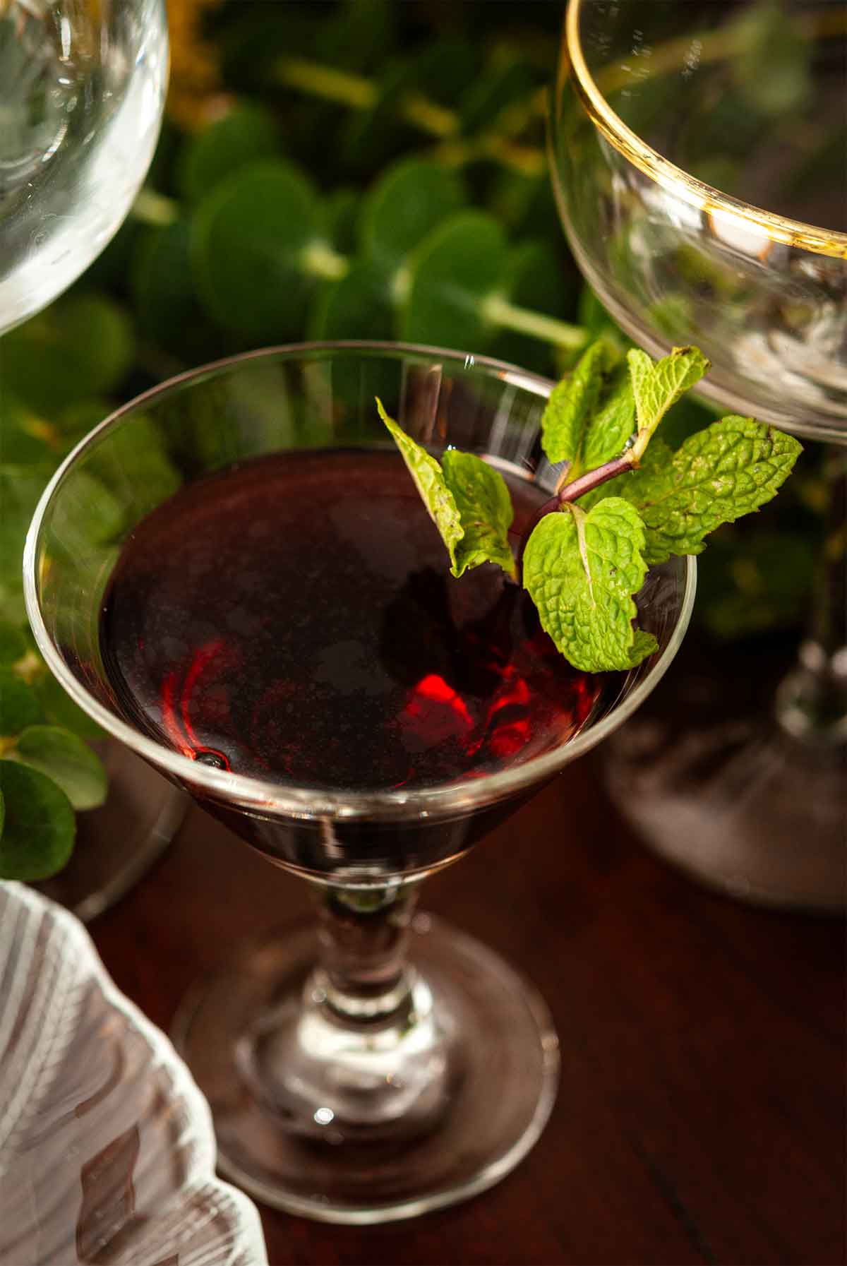 A cordial glass filled with Sorel Liqueur, garnished with mint on a table.