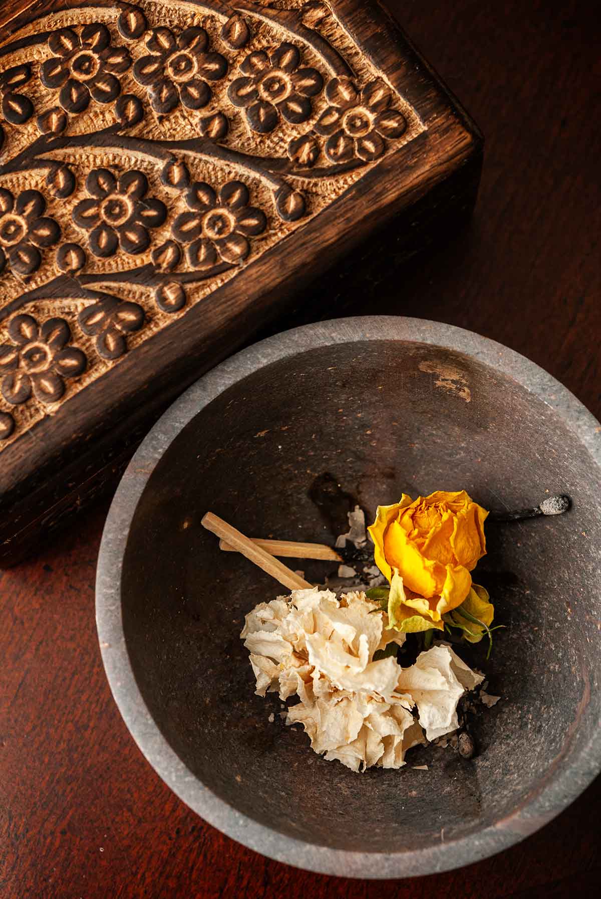 A bowl beside an ornate wooden box filled with ashes and dry flowers.