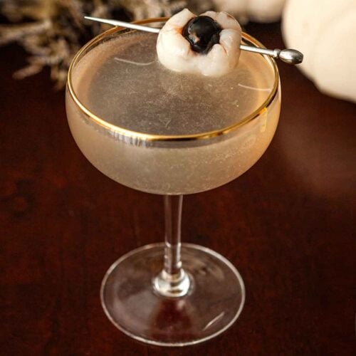 A cocktail garnished with a lychee eyeball on a table.