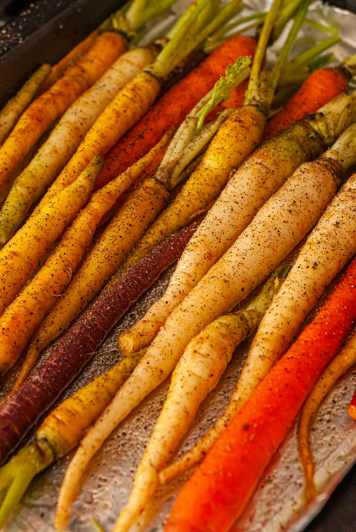 Rainbow carrots on a foil-lined baking sheet, sprinkled with salt and pepper.