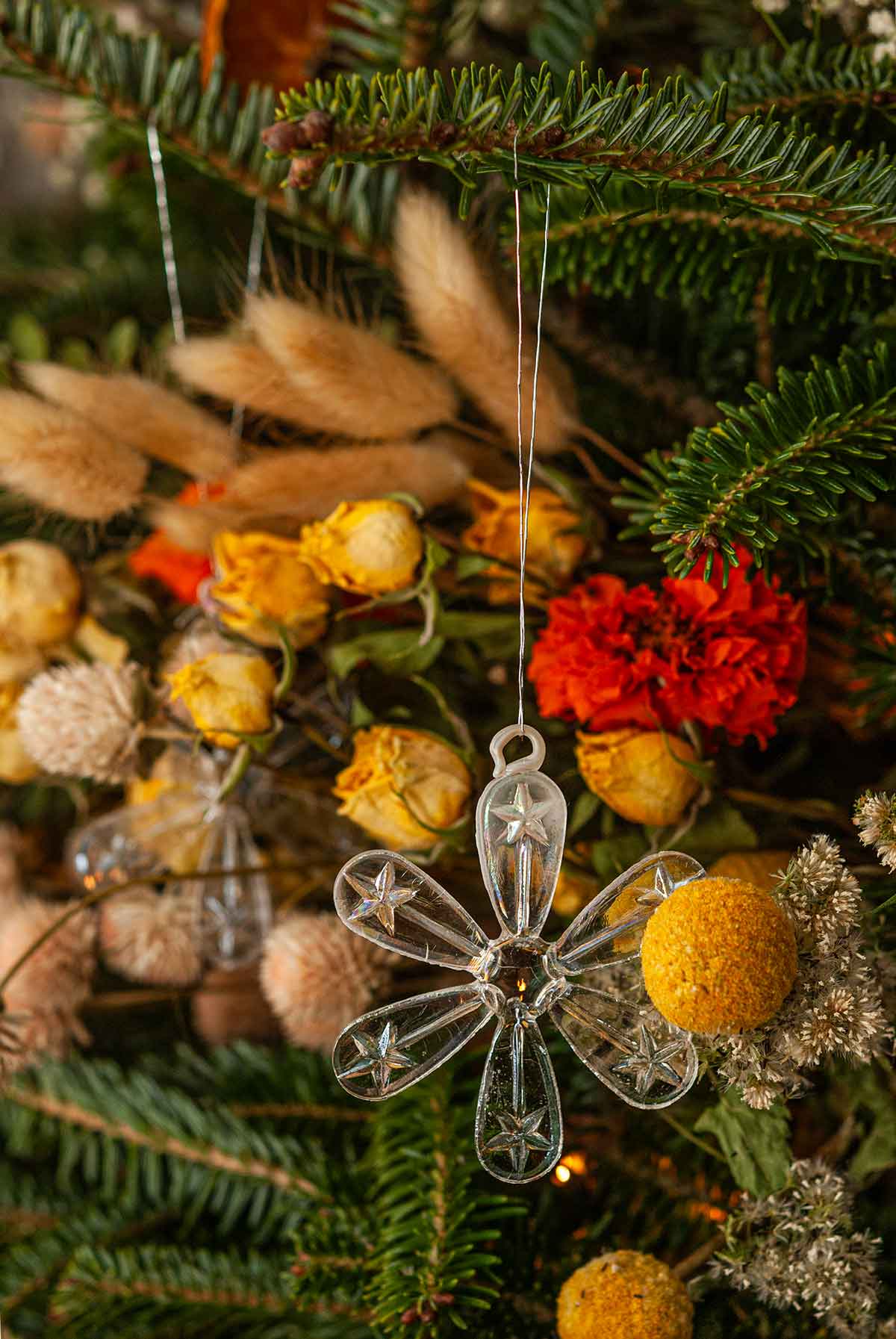 A glass snowflake ornament in front of flowers on a Christmas tree.