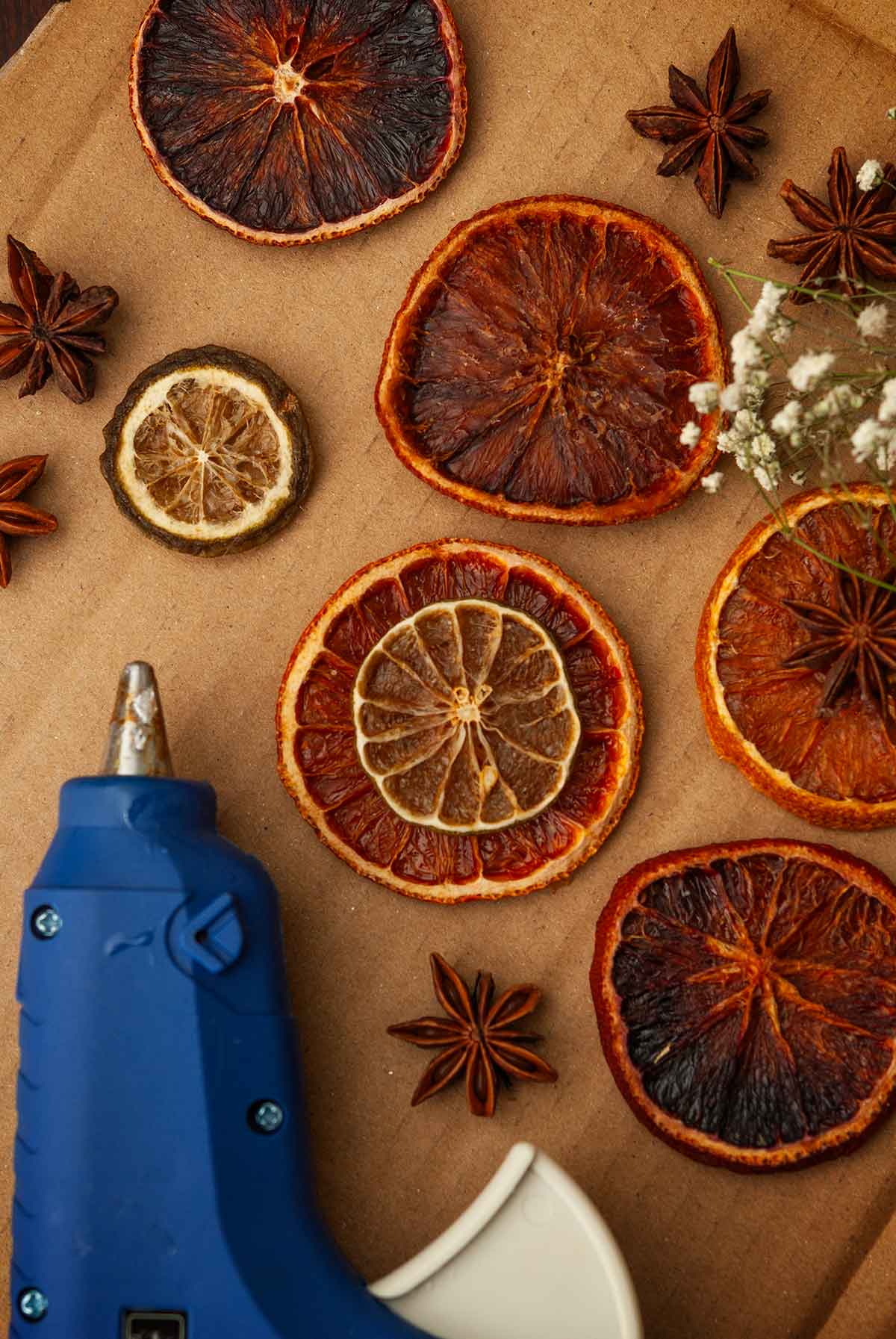 dry citrus ornaments beside a glue gun on cardboard.