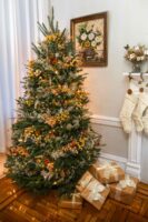 A rose and marigold Christmas tree beside presents and hanging stockings on a mantle.