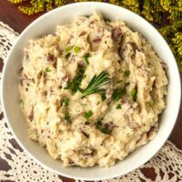 A bowl of mashed potatoes on a lace tablecloth with goldenrod flowers.