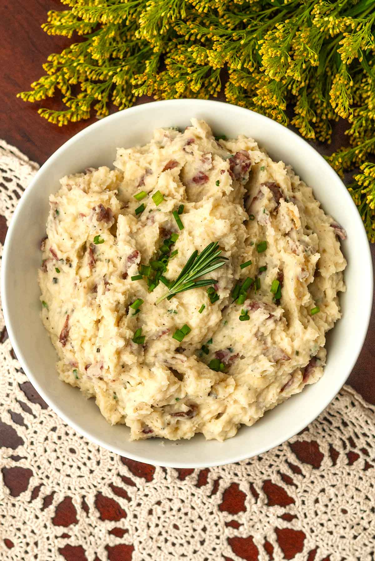 A bowl of mashed potatoes on a lace tablecloth with goldenrod flowers.