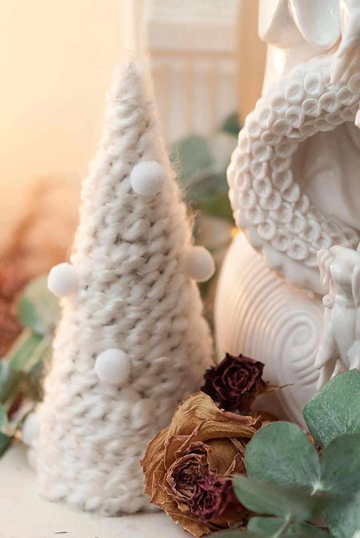A small Christmas tree made of yarn on a mantle decorated with dry roses and eucalyptus.
