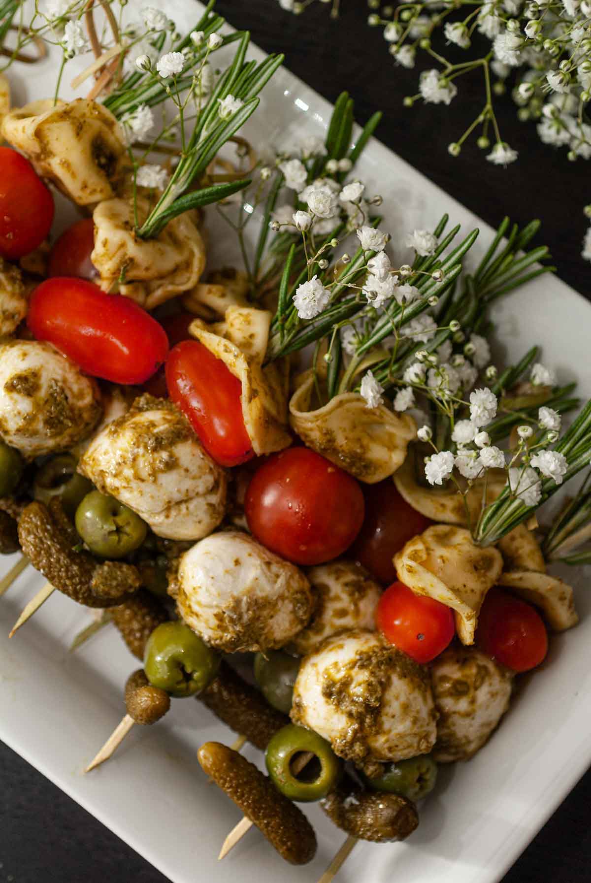 Antipasto skewers garnished with flowers and rosemary stacked on a plate.