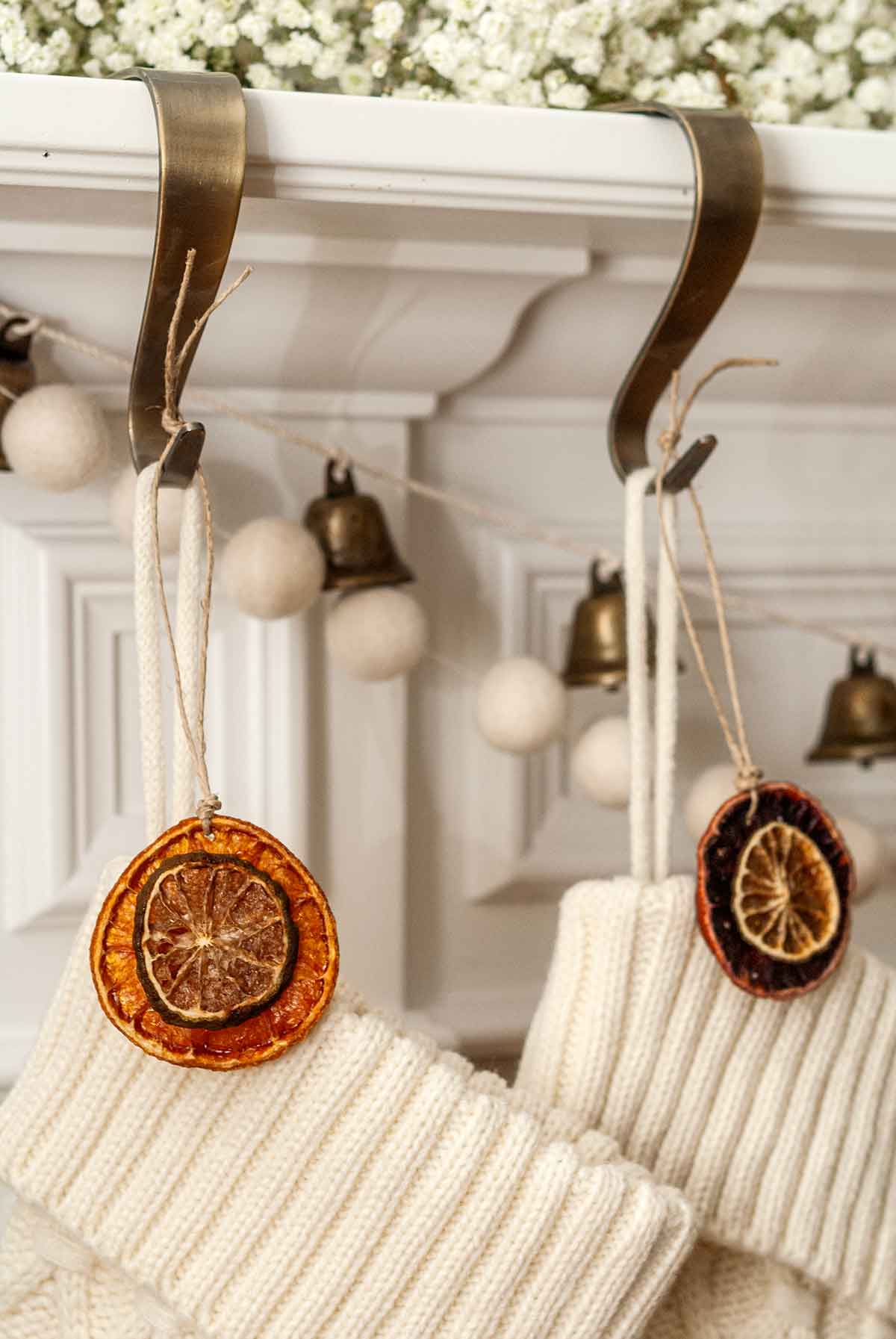 The citrus ornaments hung atop 2 christmas stockings hanging from a mantle.