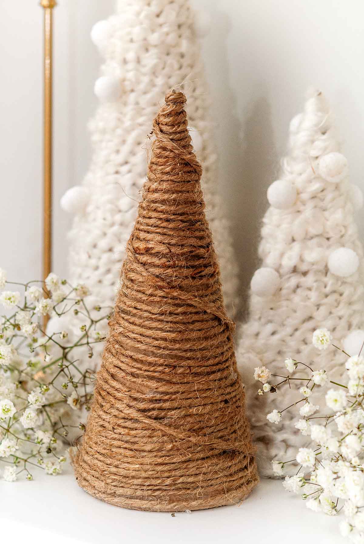 3 wool and twine tree decorations on a mantle beside baby's breath.