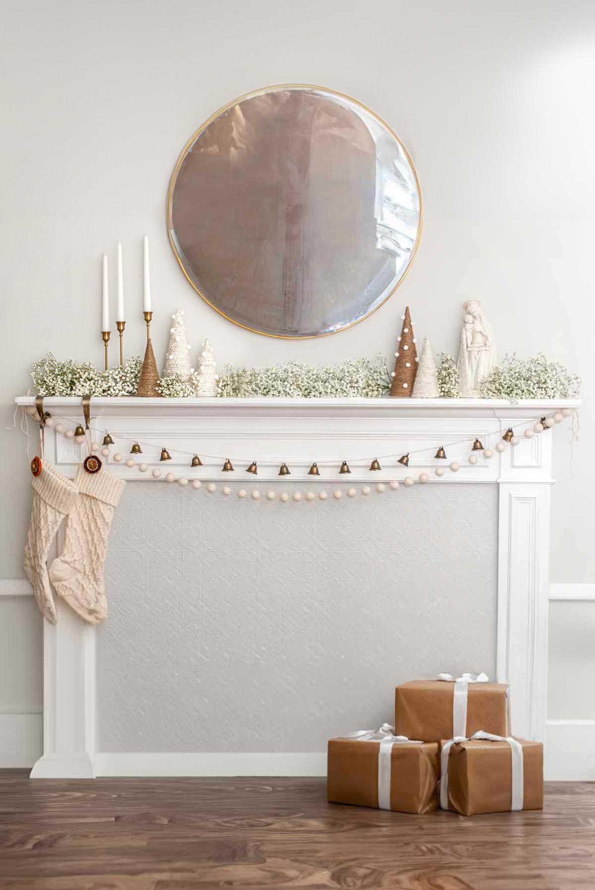 A minimally designed Christmas mantle with baby's breath and presents on the ground.