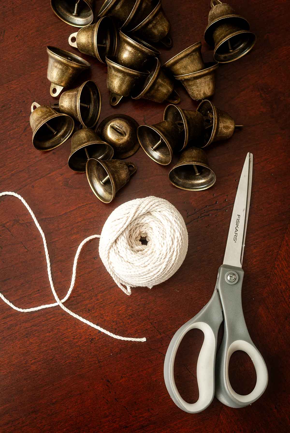 Scissors, a spool of baker's string, and about 20 bells on a table.