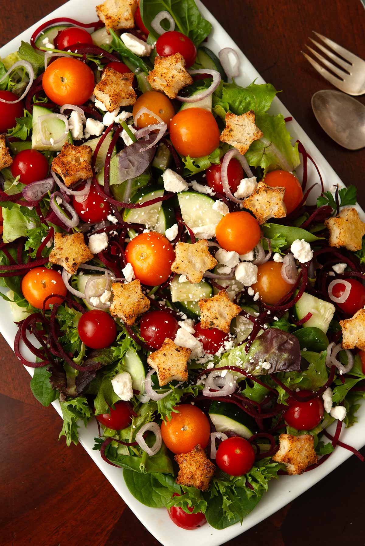 A salad with star-shaped croutons on a table beside a spoon and fork.