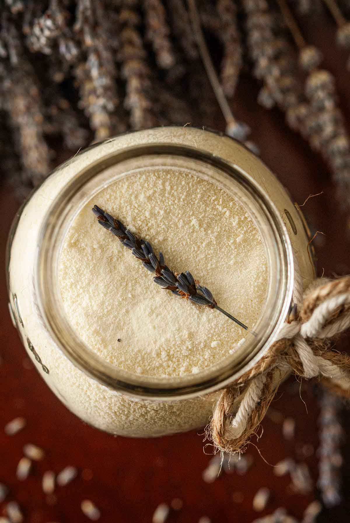 A sprig of lavender in a jar of powdered milk on a table.
