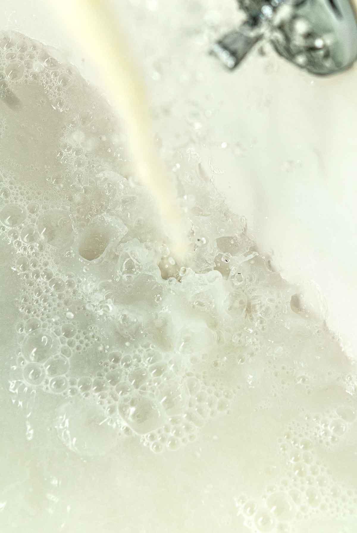 Powdered milk pouring into the stream of a running faucet in a bath tub.