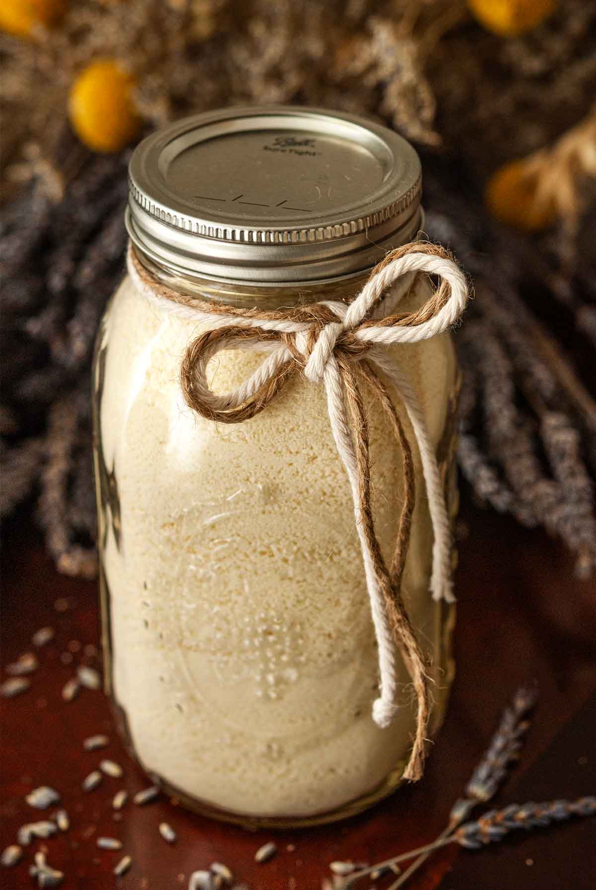 A jar tied with 2 strings in front of a large bouquet of lavender on a table.