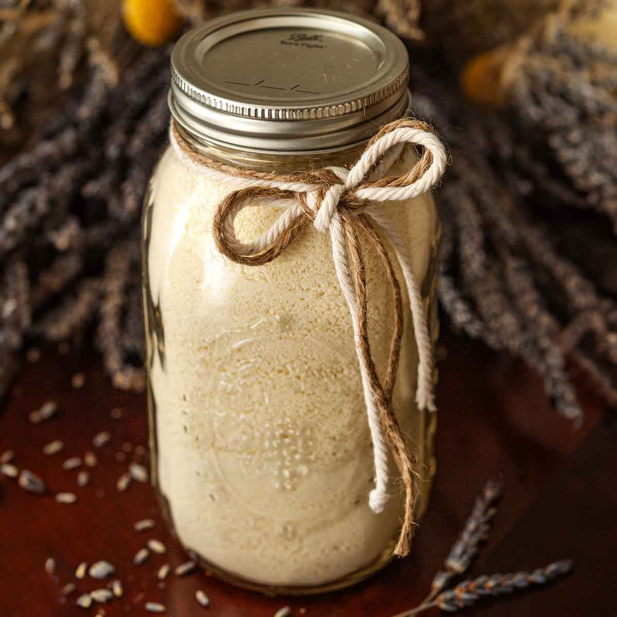 A jar tied with 2 strings in front of a large bouquet of lavender on a table.