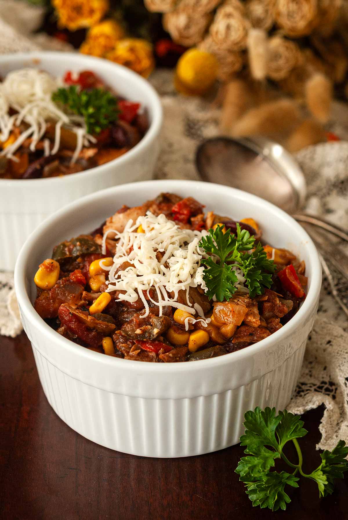 2 bowls of turkey chili on a table in front of flowers, garnished with cheese and parsley.