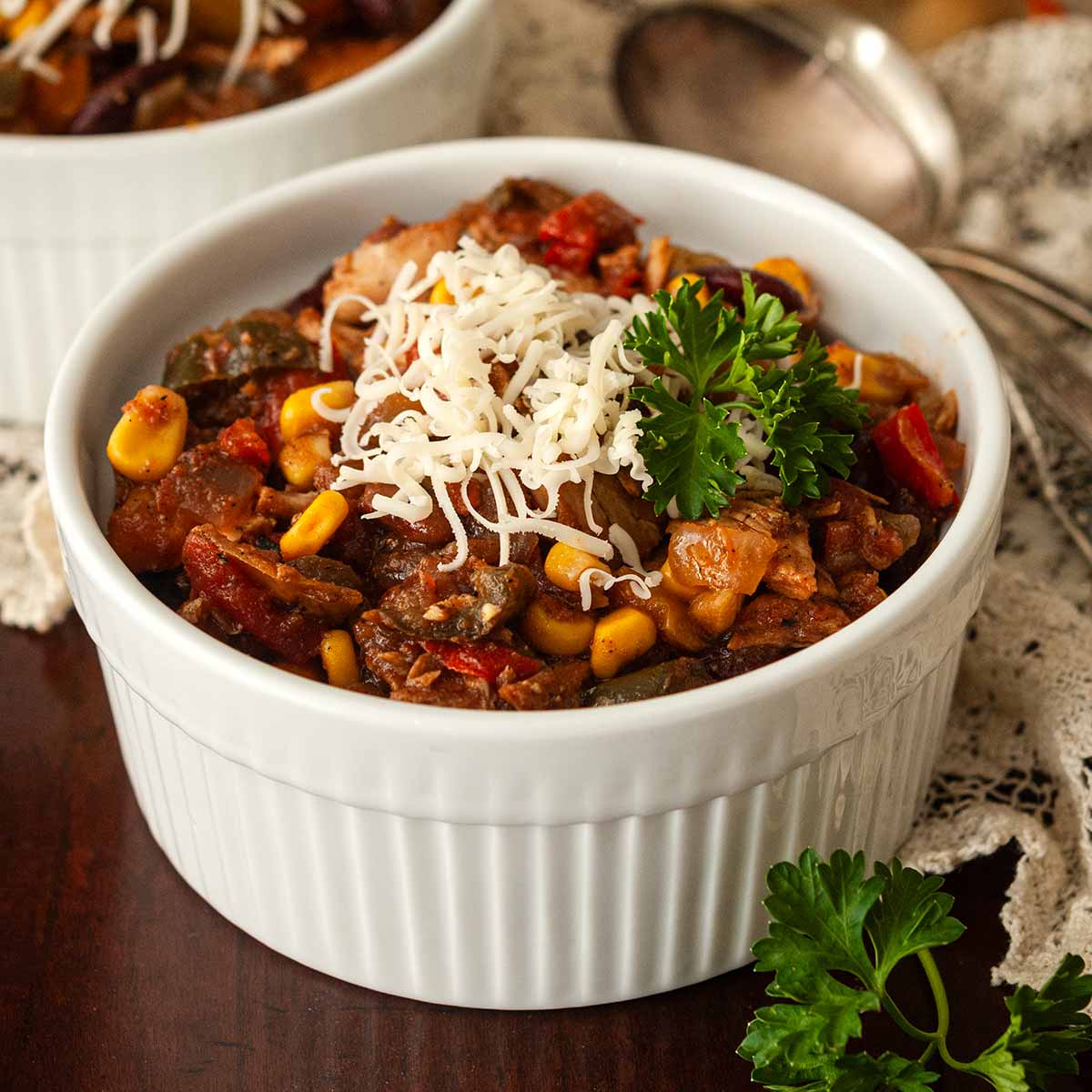 A bowl of turkey chili on a table garnished with cheese and parsley.