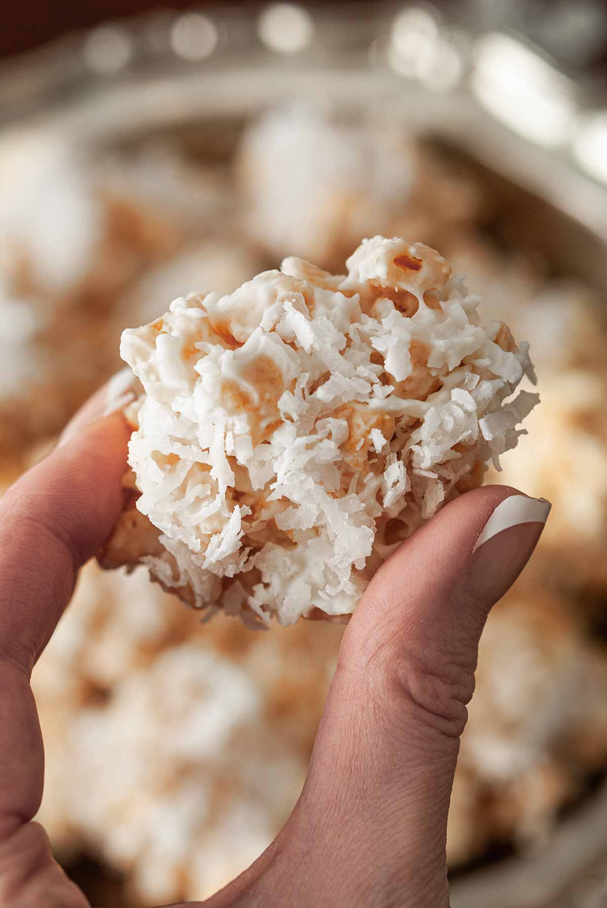 Fingers holding a cookie covered in coconut.