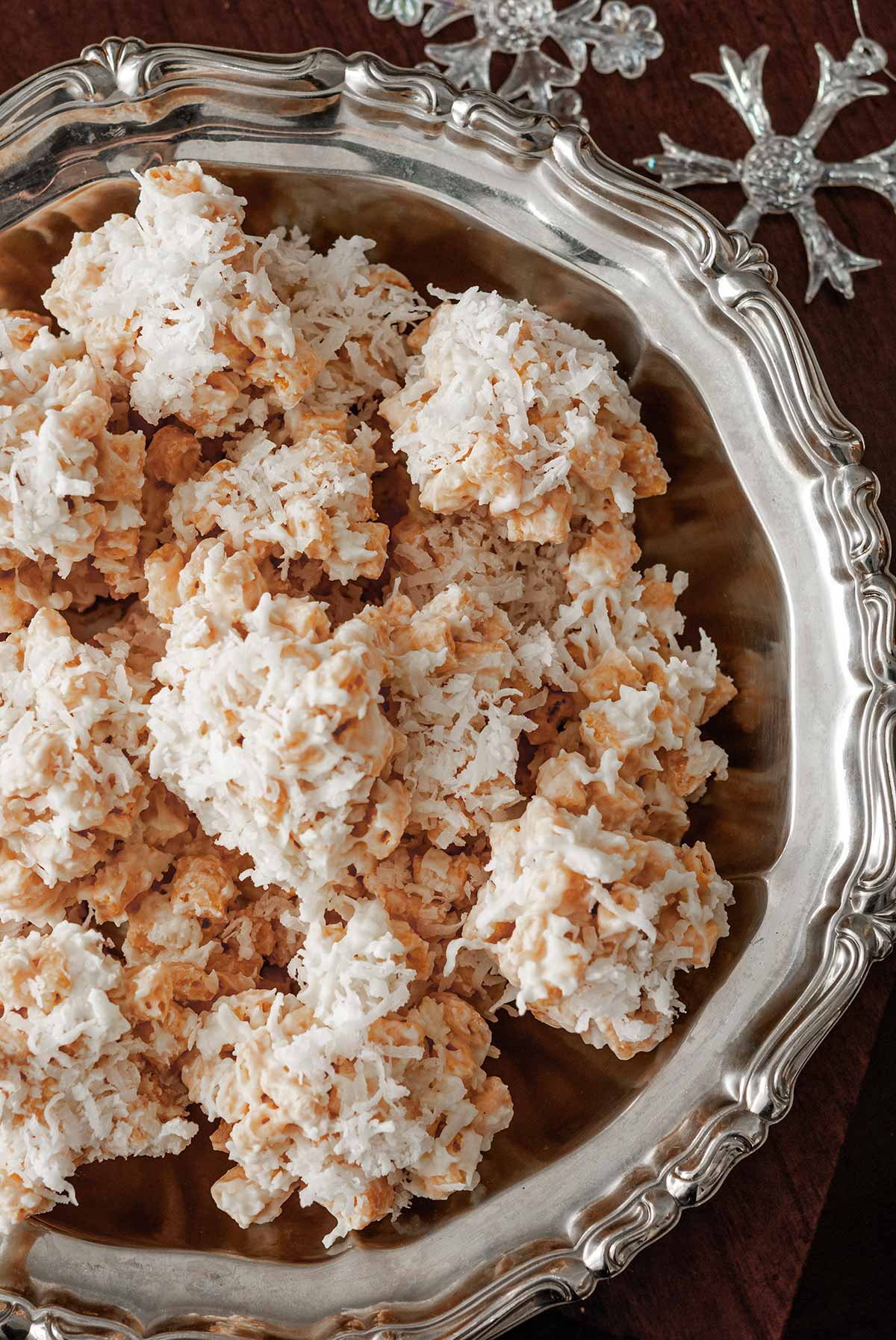 Coconut cookies in a decorative silver bowl with 2 glass snowflake ornaments on a table.