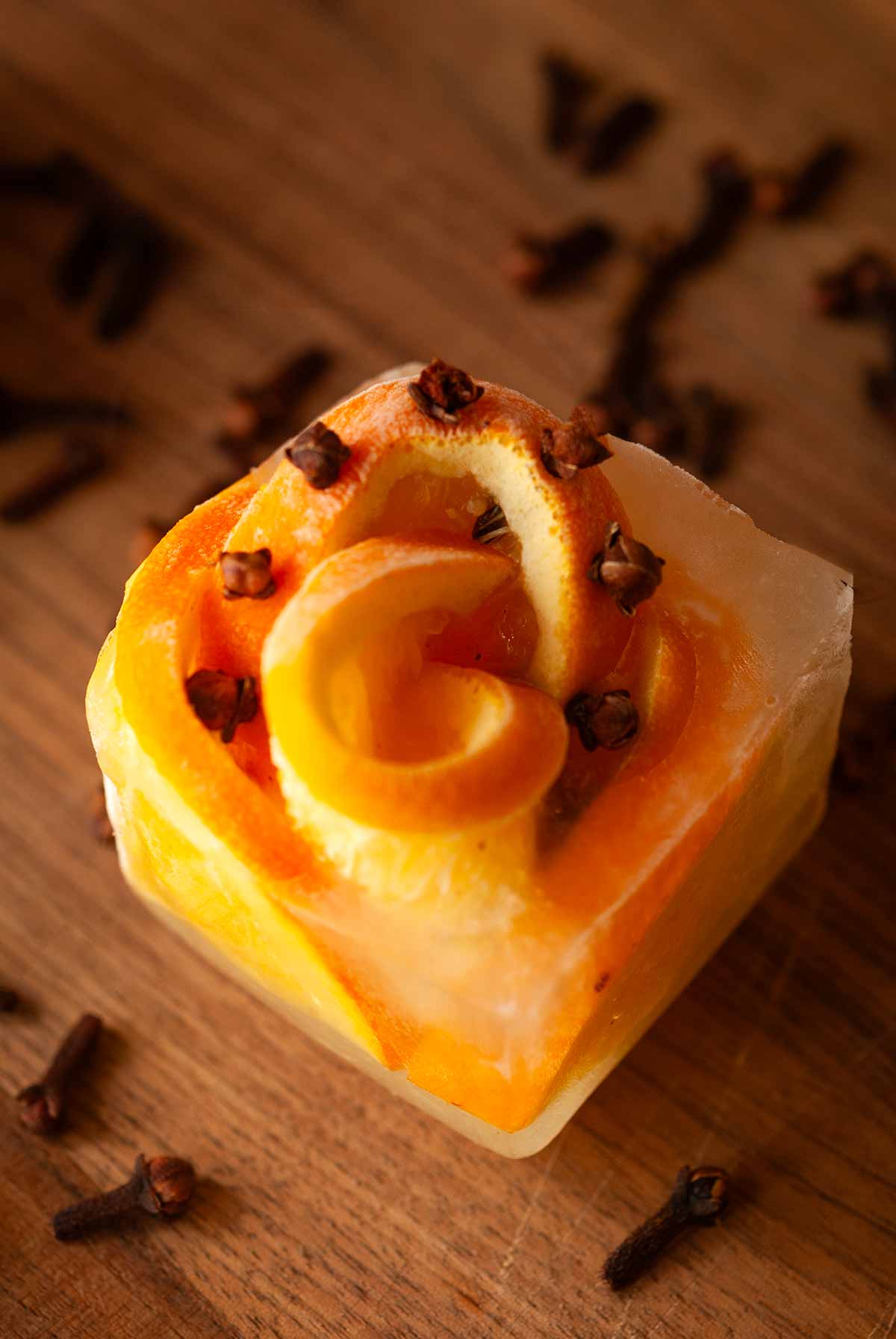 1 clove orange ice cube on a cutting board surrounded by cloves.