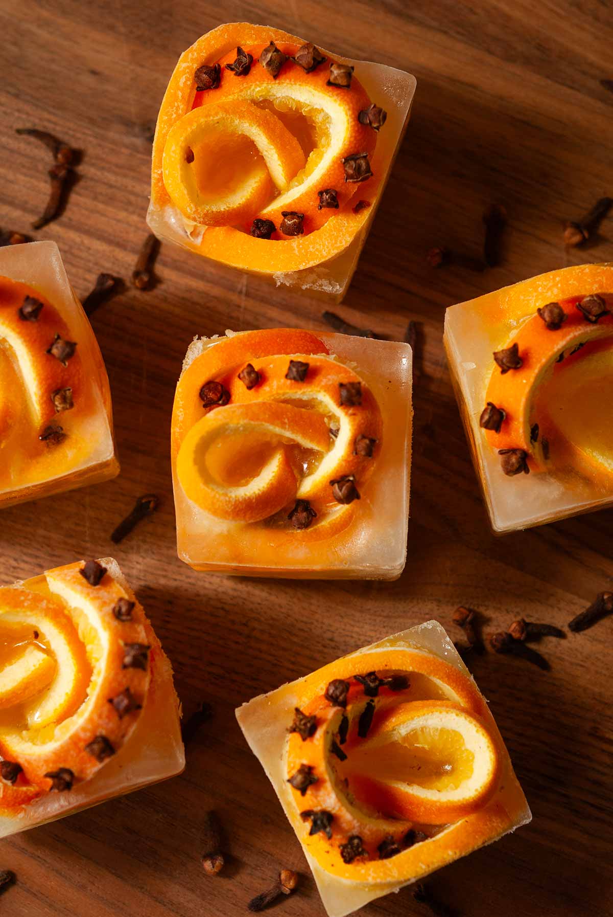The top of 6 clove orange ice cubes surrounded by cloves.