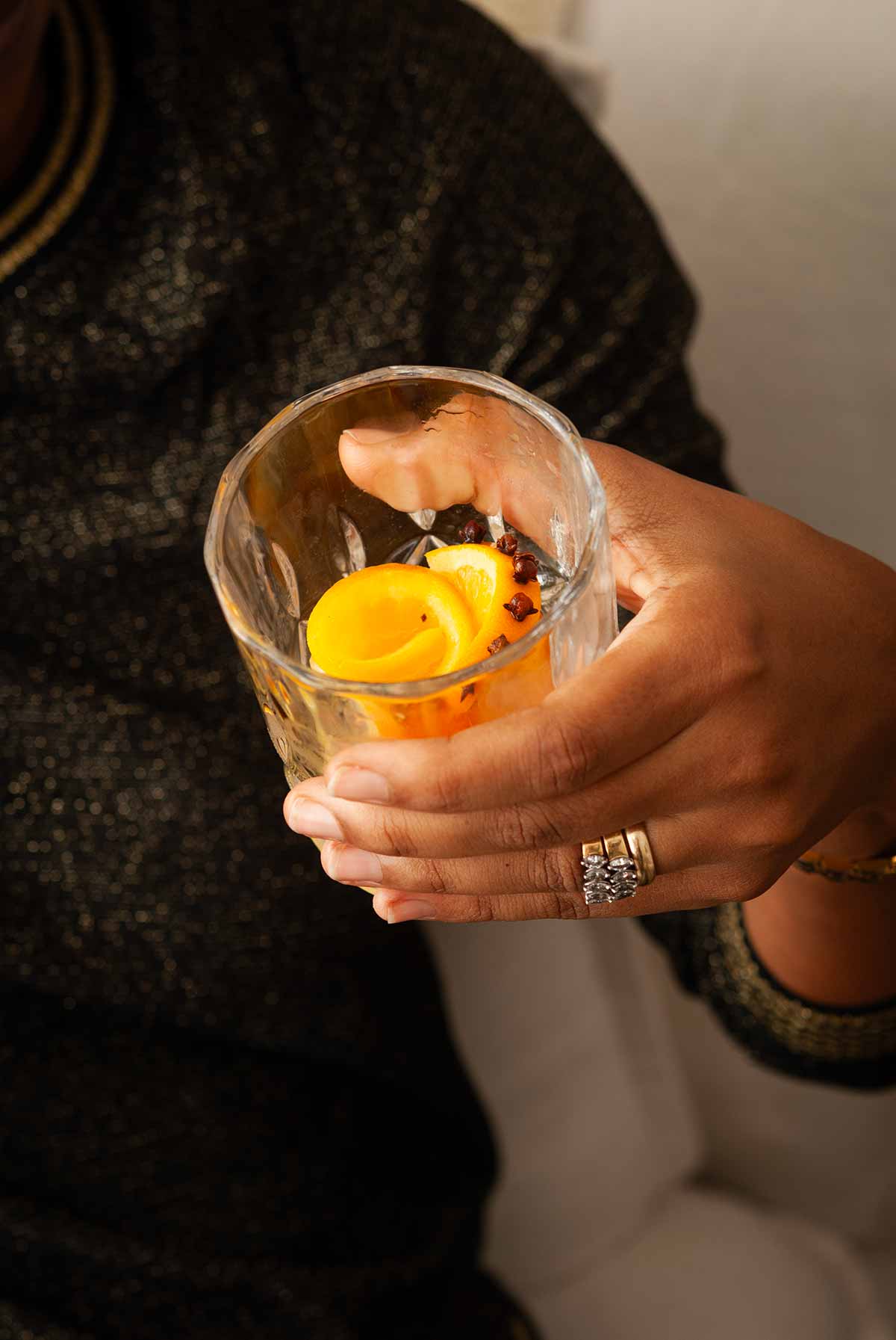 A hand holding a cocktail, showing the orange rose garnish.