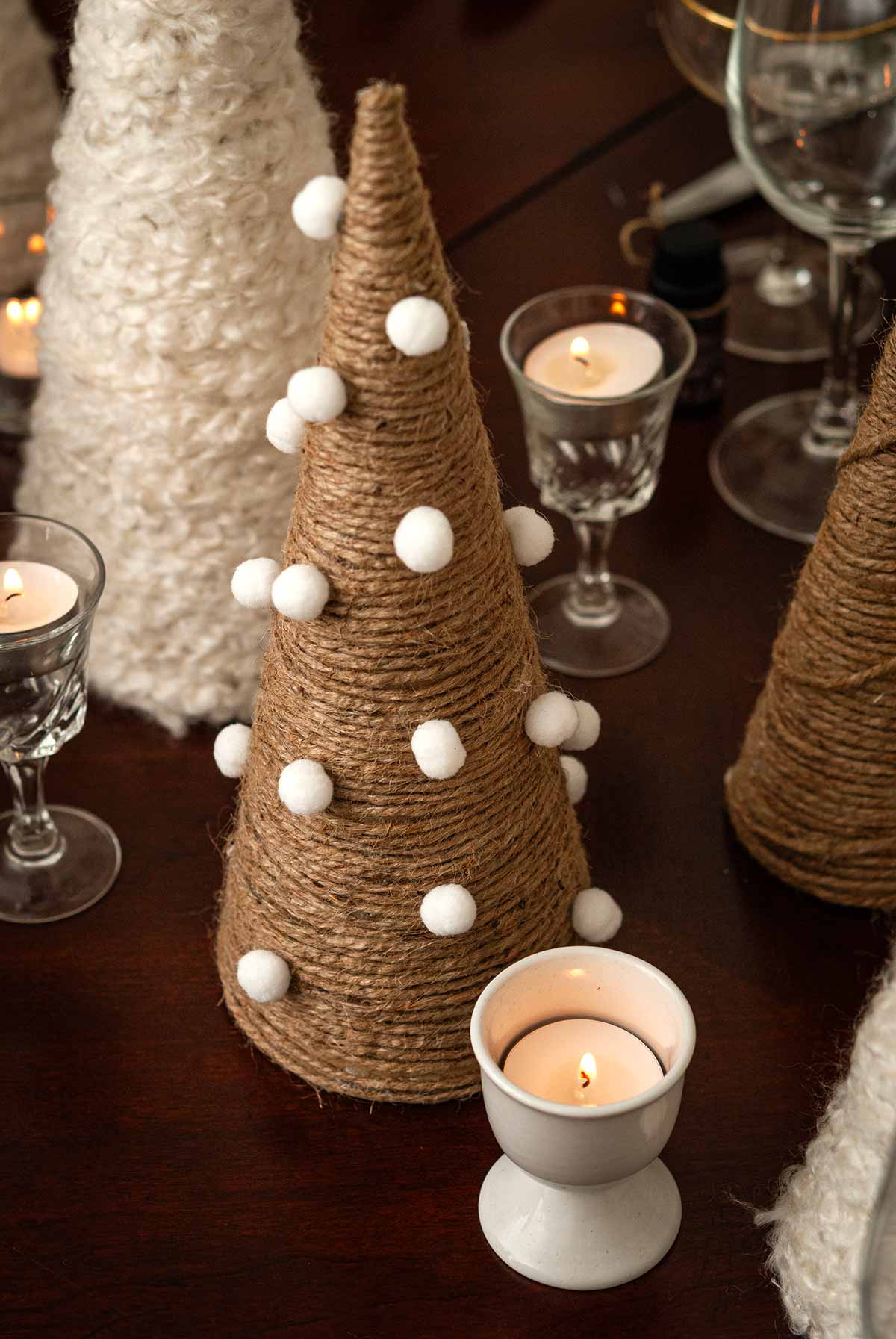 A twine tree with tiny pompom balls next to an egg cup tea light on a table.