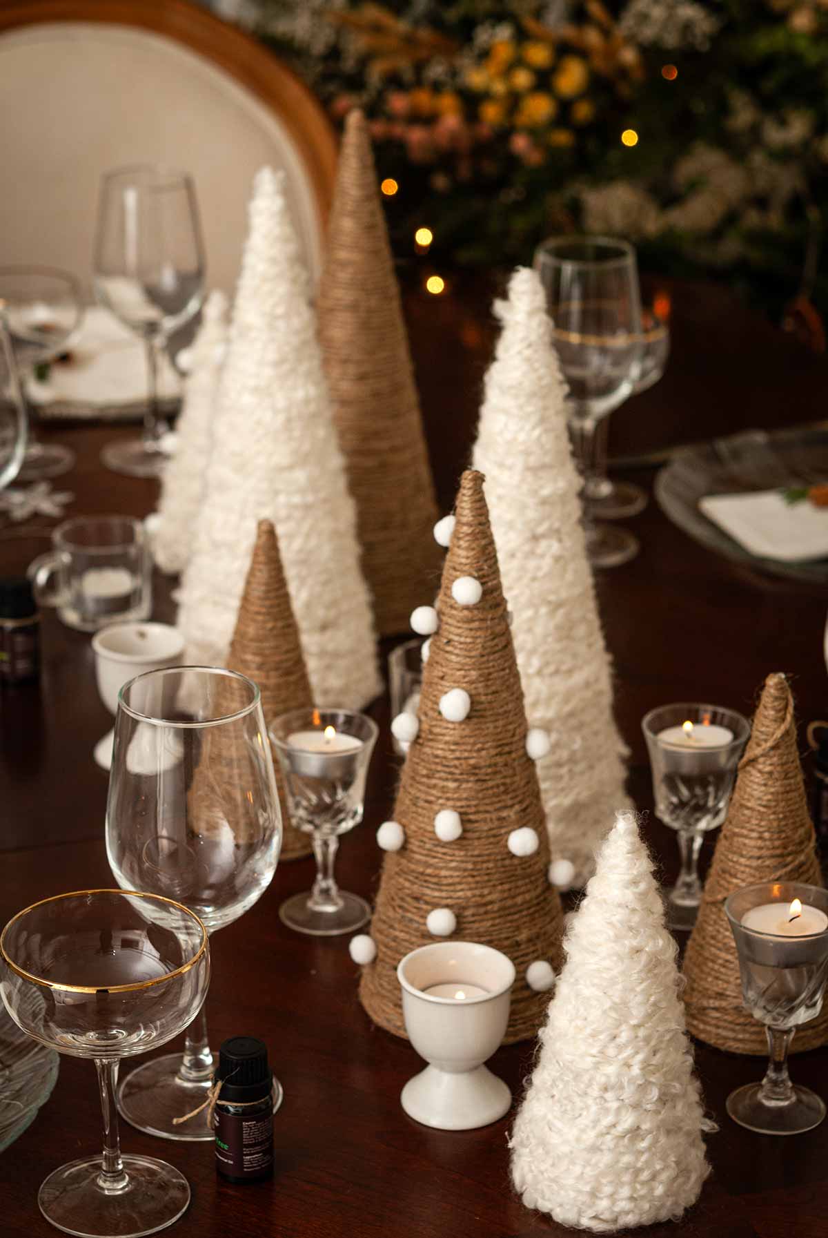 Trees made of twine and wool on a set dining table i front of a christmas tree.