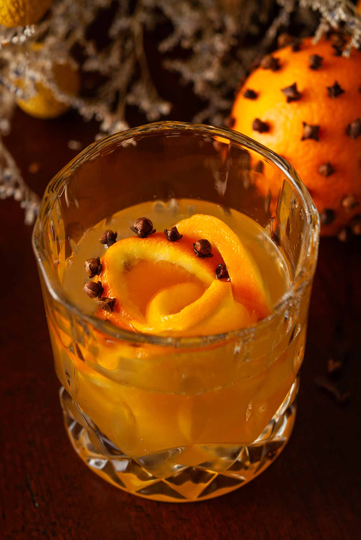 A cocktail in front of a clove orange with a clove orange rose ice cube.