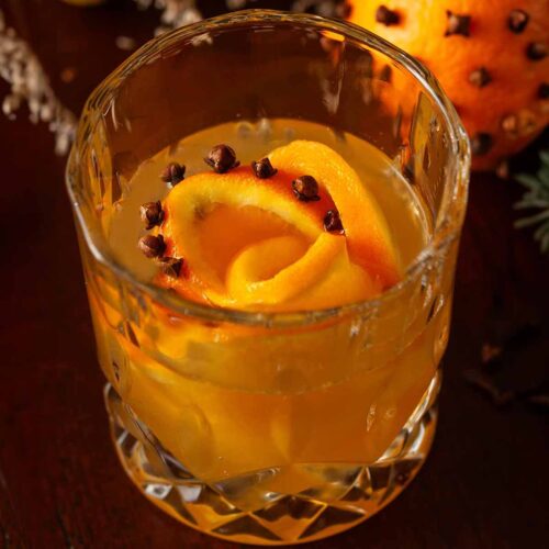 A cocktail in front of a clove orange with a clove orange rose ice cube.