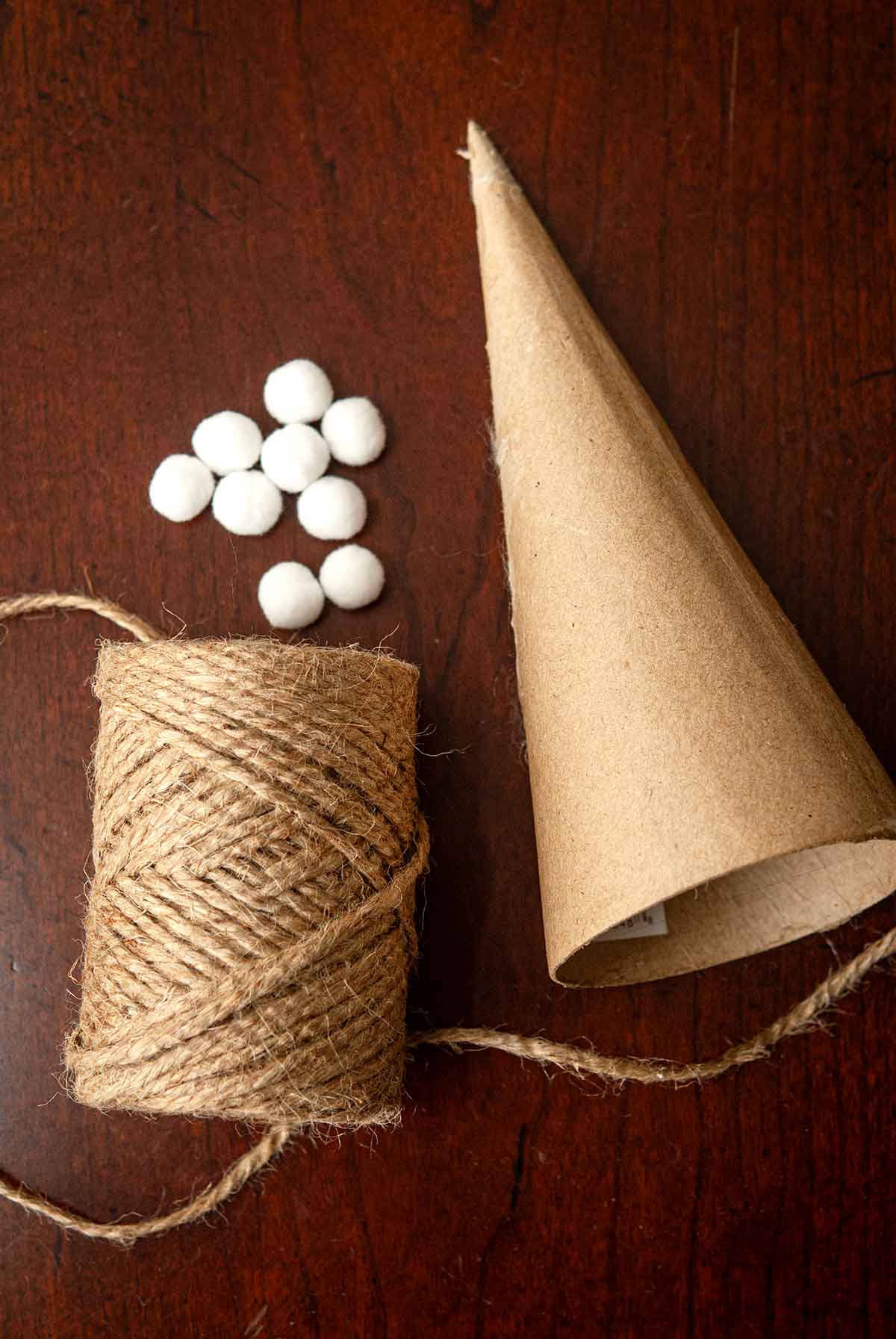 A paper mache cone, about 10 small pompoms, and a spool of twine on a table.