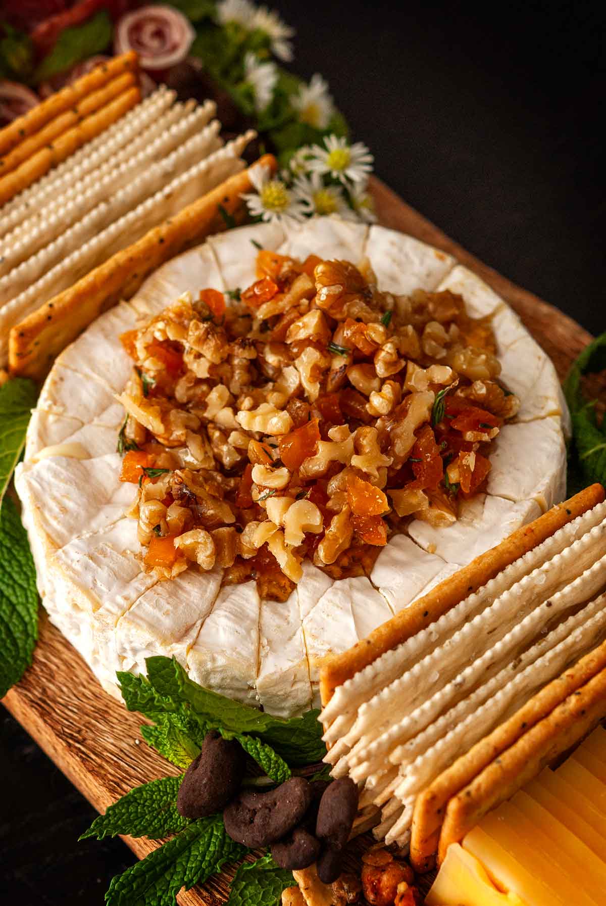 Chopped apricots, walnuts and thyme with honey on top of brie on a cheeseboard.