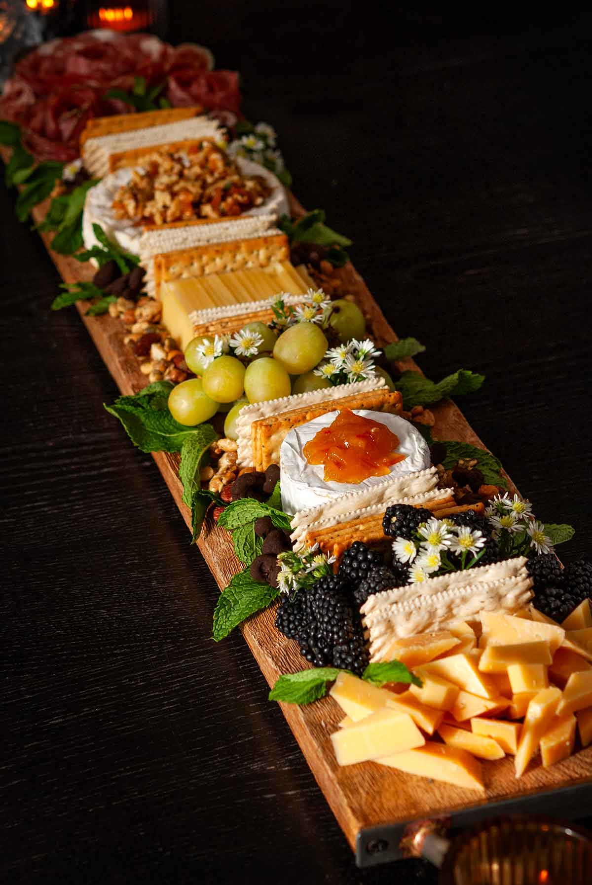 A fancy cheese board with 4 cheeses, crackers, berries, grapes and meat roses.