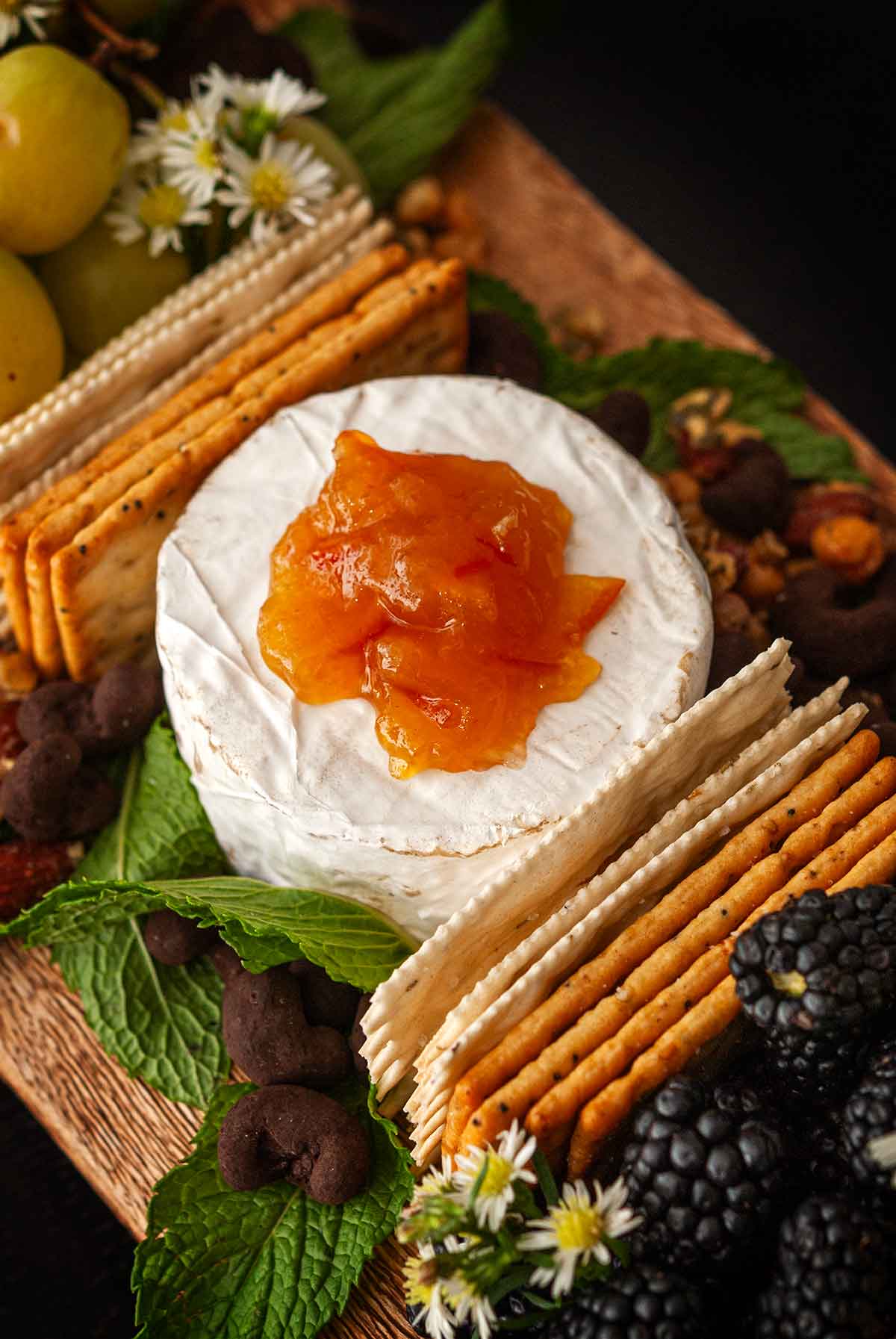 Cheese on a board, topped with marmalade, surrounded by crackrs and mint.