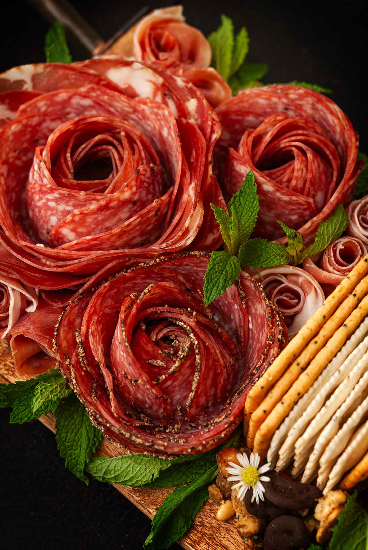 Meat roses on the end of a cheese board with mint and crackers.