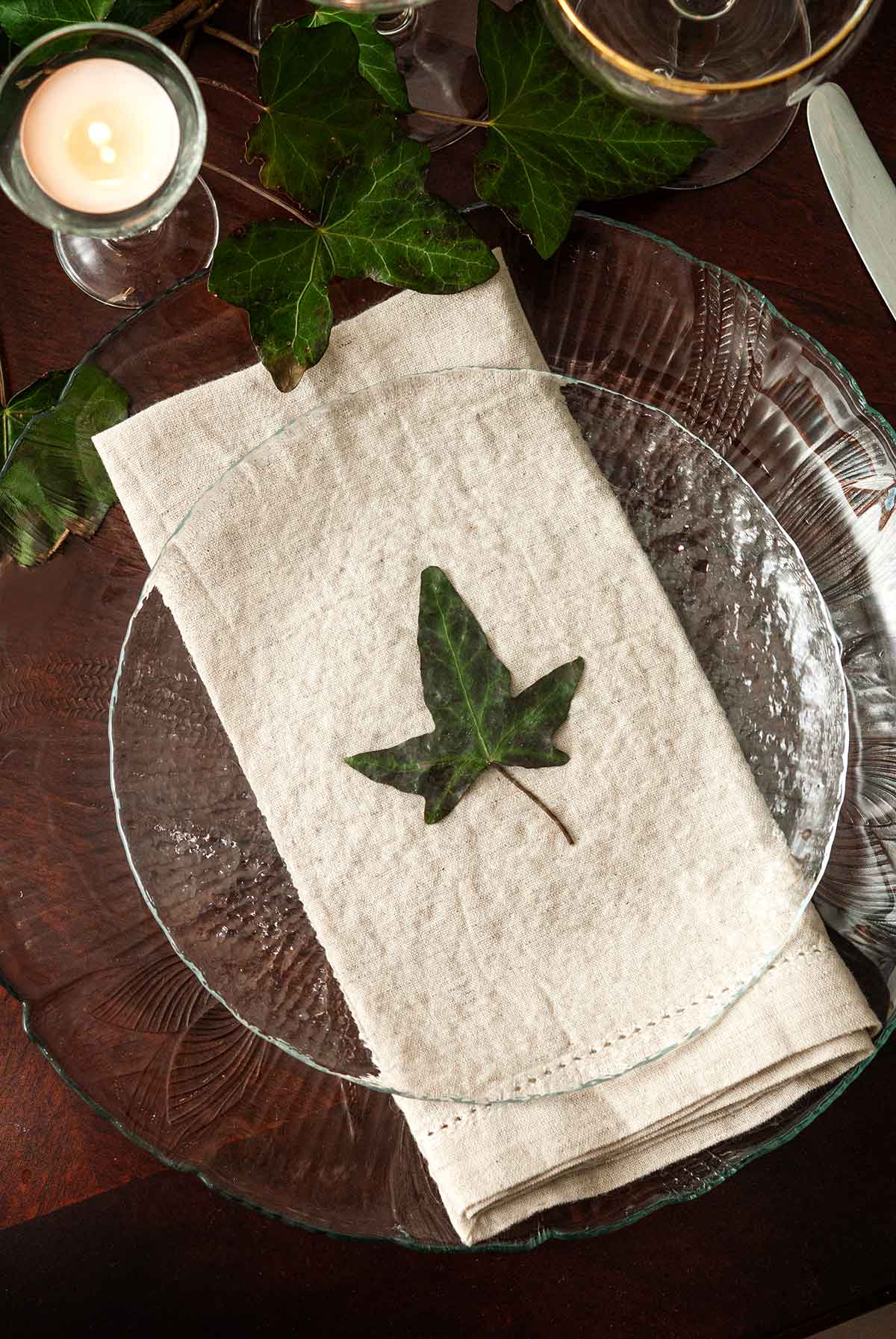 An ivy leaf in the center of a plate on top of a napkin on a table with ivy.