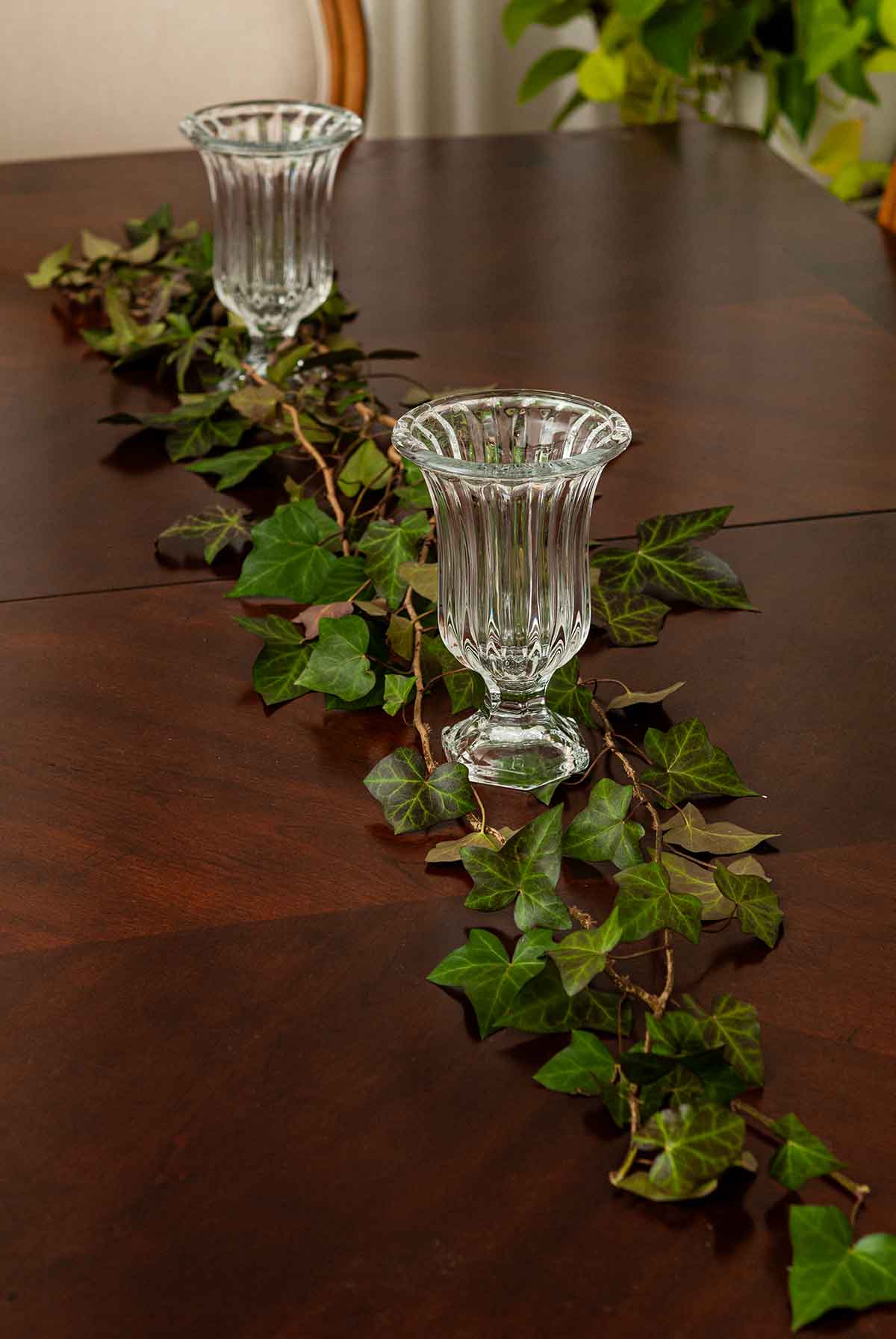 A table with 2 vines of ivy and 2 glass vases.
