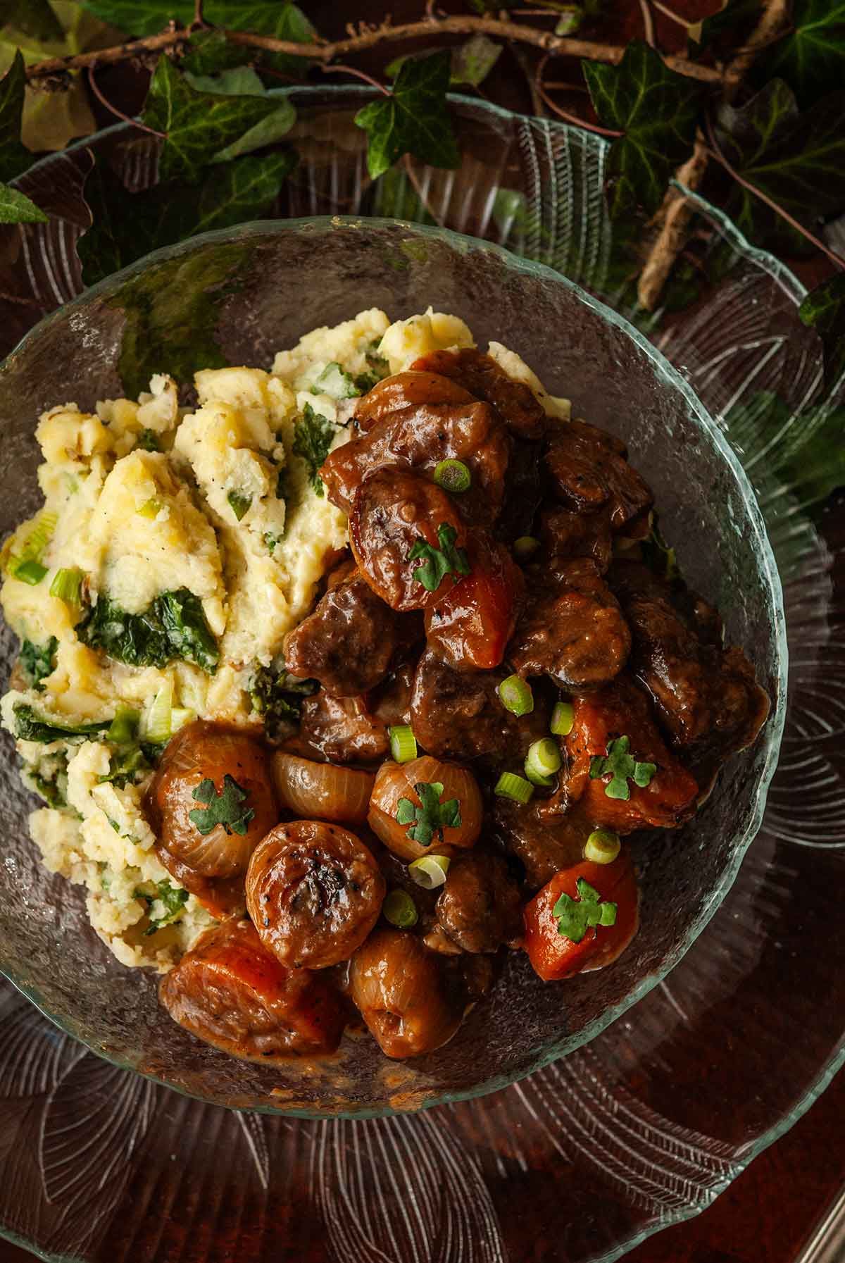 The top of Lamb stew on top of potatoes with kale on a plate surrounded by ivy.