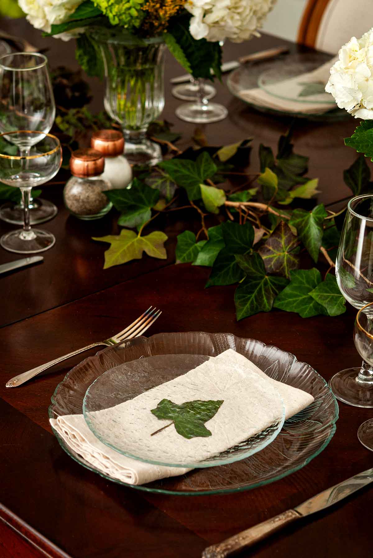 2 plates with an ivy leaf between them on a table decorated with ivy.